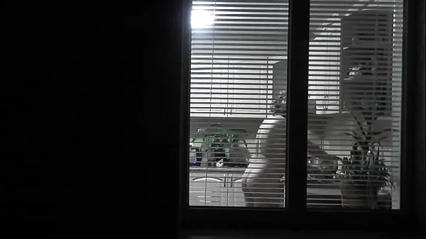 Peeping. Voyeur. Neighbor pervert voyeur in evening on street looks out window as naked sexy neighbor in kitchen prepares dinner for her husband. Naked in public. Naked at home. Family.  Outdoor